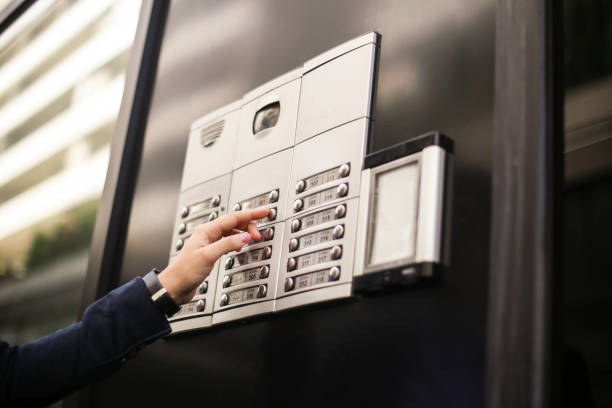 Unrecognizable Caucasian female using an intercom with camera - door security on a building.